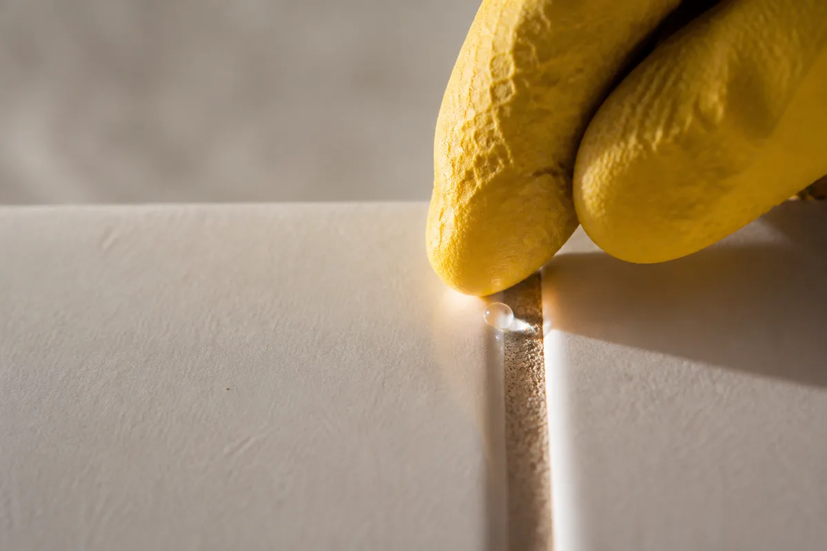 Main gantée déposant une goutte d’eau sur un joint de carrelage mural pour tester sa porosité