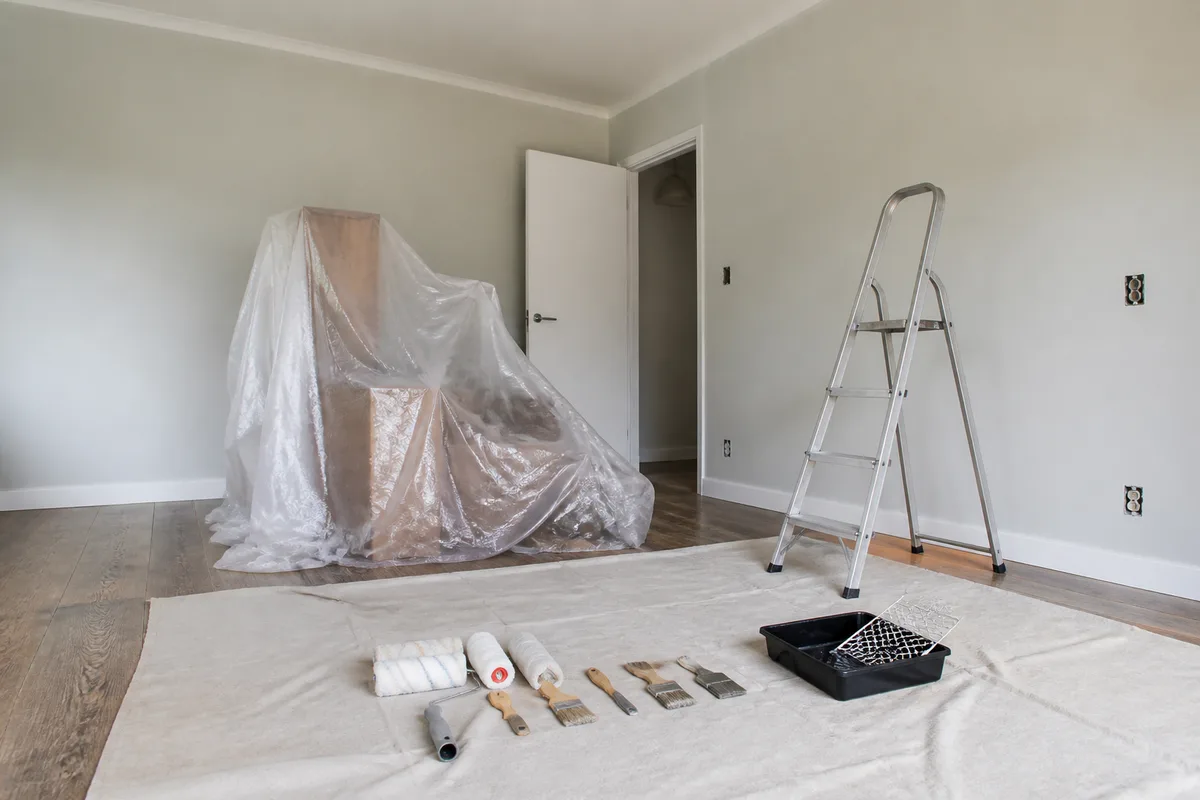 Pièce vidée et bâchée avant travaux de peinture, escabeau et matériel posés au centre