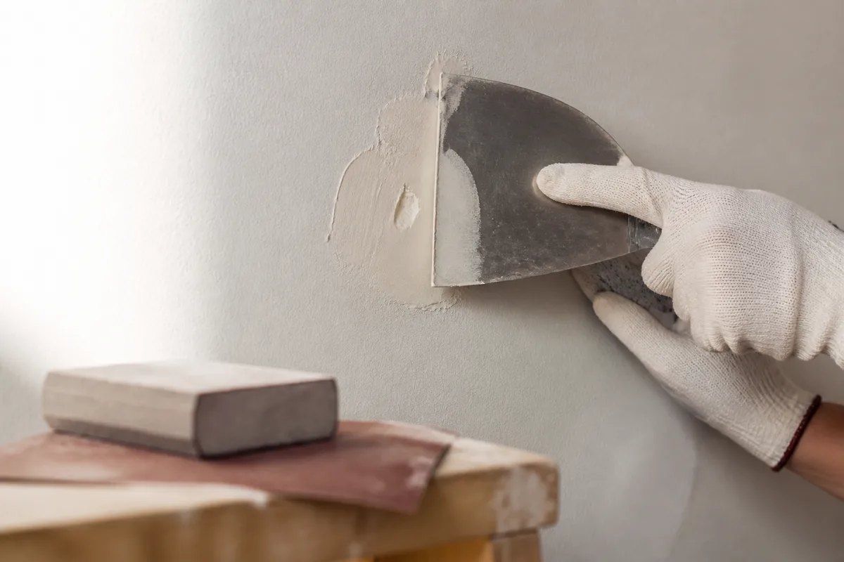 Mains gantées appliquant de l&rsquo;enduit de rebouchage au couteau sur un mur intérieur