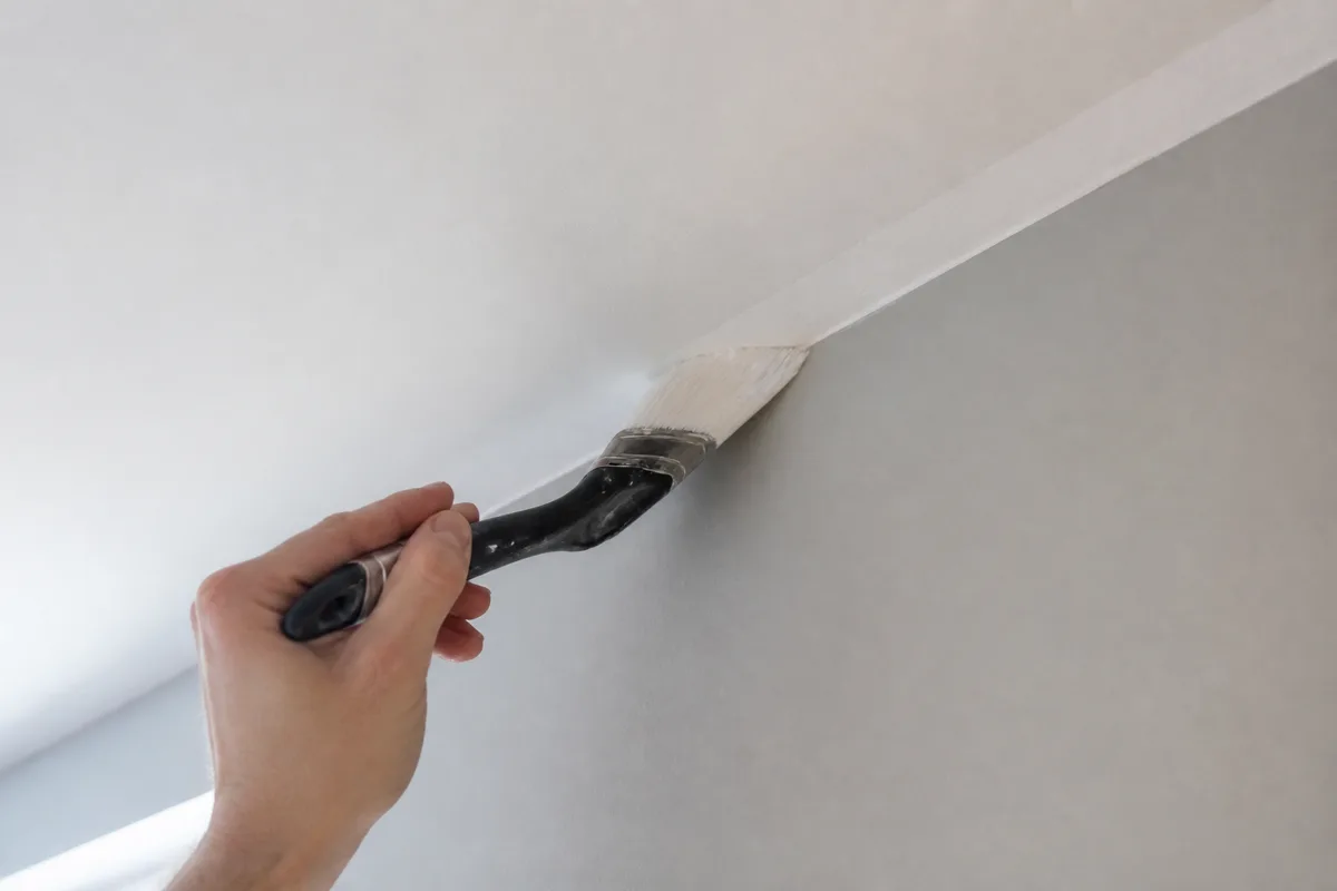 Rechampi au pinceau coudé dans l&rsquo;angle entre un mur et un plafond fraîchement peint